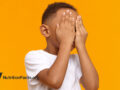 young boy covering his face against orange background