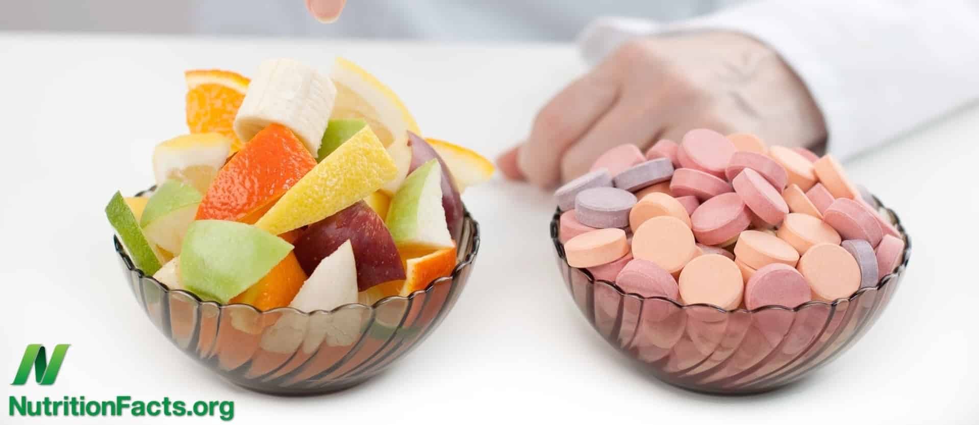 a bowl of cut-up fruit alongside a bowl of various pills