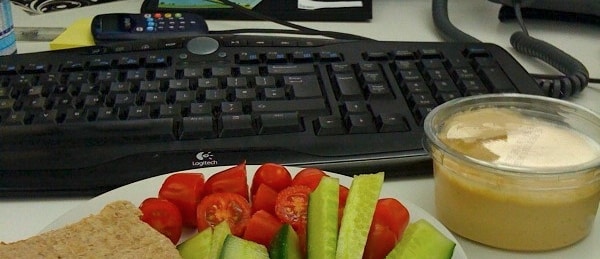 plate of sliced vegetables and tub of hummus on a work desk