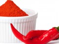 ramekin of cayenne pepper powder alongside two fresh cayenne peppers