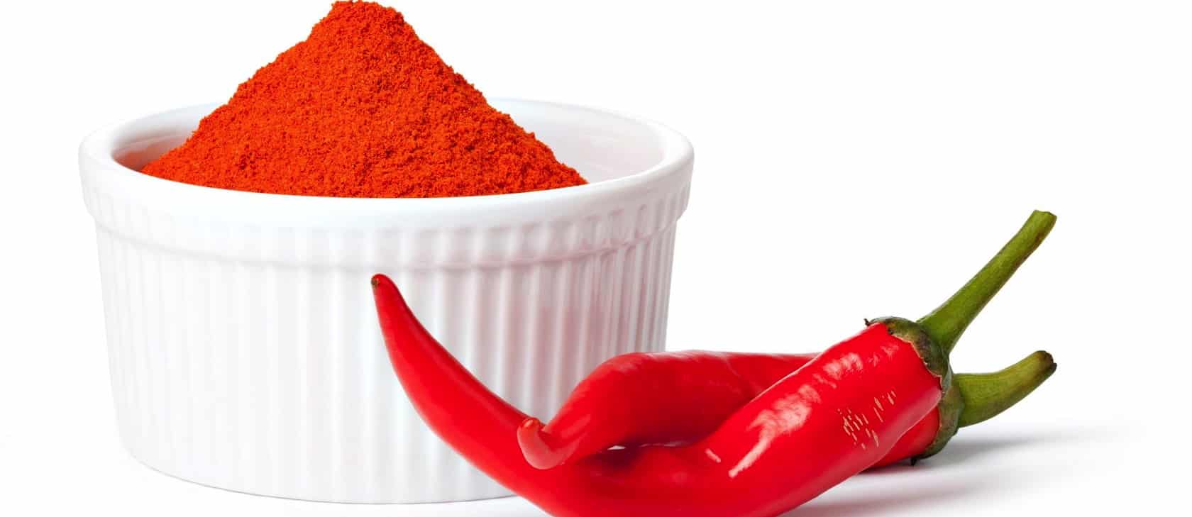 ramekin of cayenne pepper powder alongside two fresh cayenne peppers
