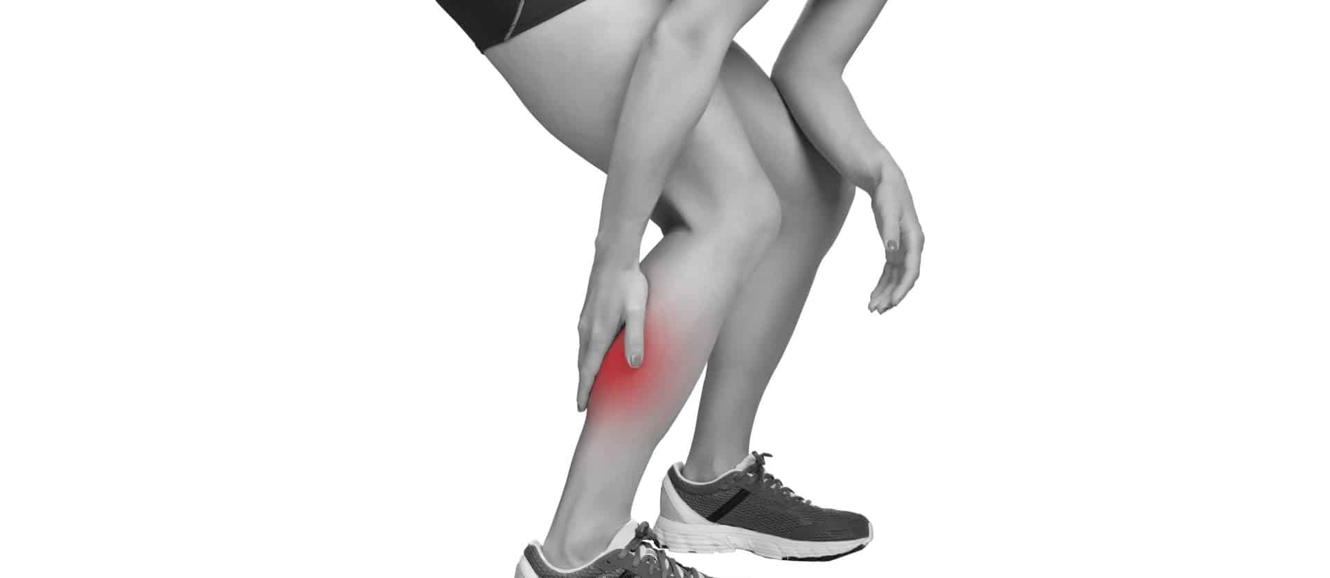 black and white image of a person grabbing their calf that is shaded red