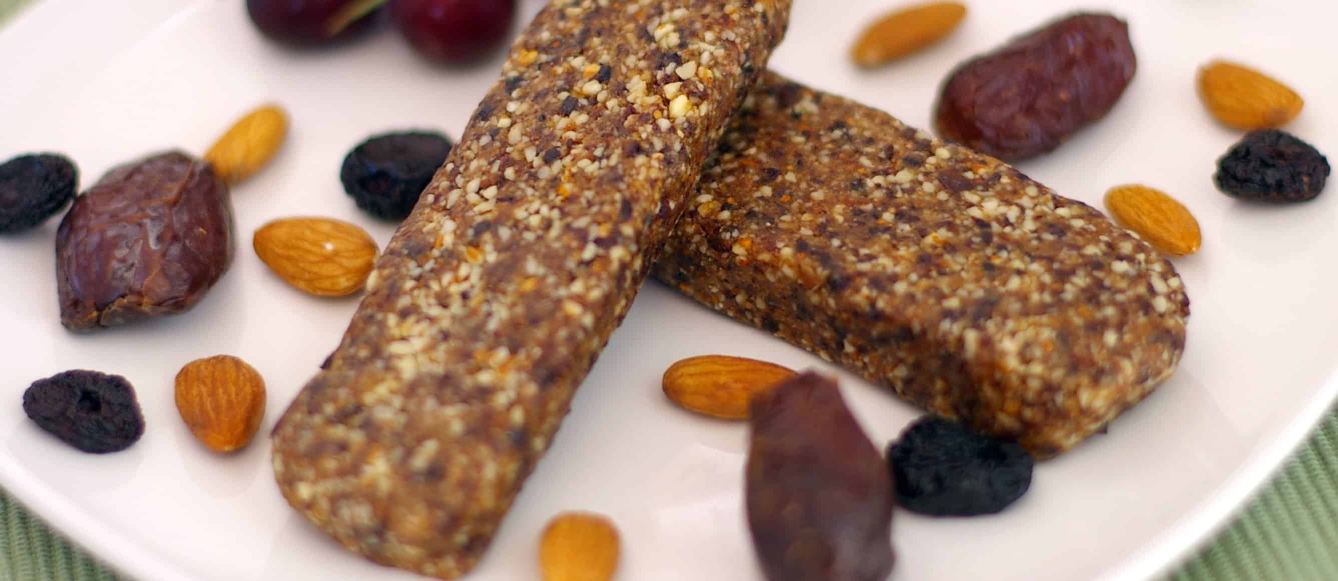 two nut and seed bars on a plate with almonds and raisins
