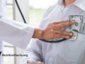 doctor with stethoscope on patient with money in pocket