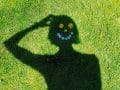 shadow of a person on grass with flowers shaped into a smiley face