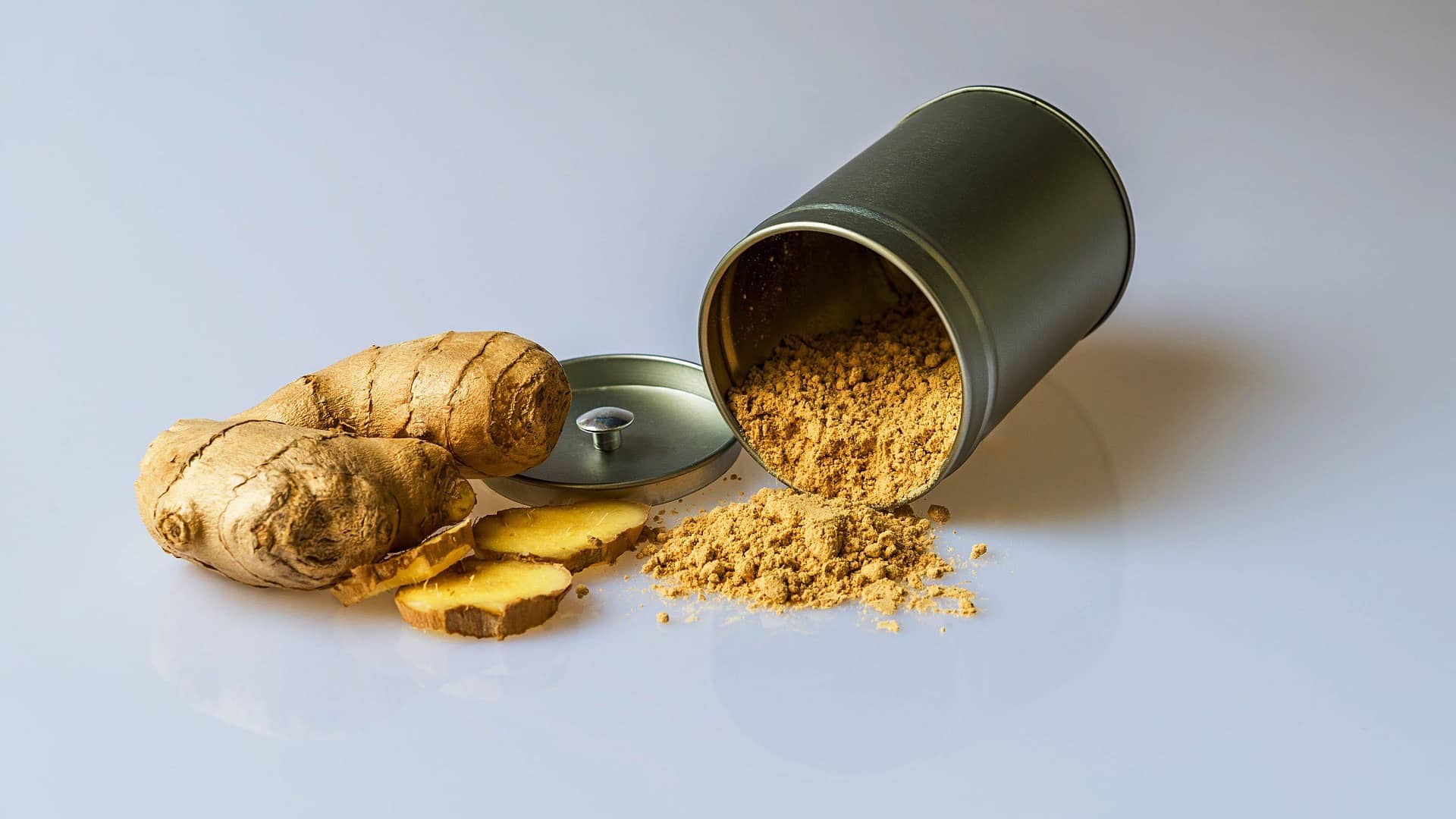 piece of fresh ginger root alongside a tub of ginger powder