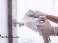 person spraying cleaner on door handle