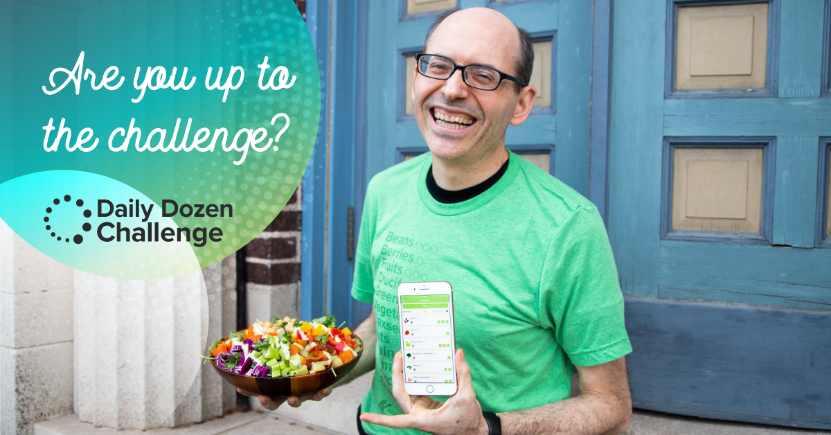 Dr. Greger holding a bowl of vegetables and a phone with the daily dozen app on it