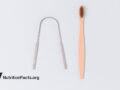 Tongue scraper and pink toothbrush on white surface