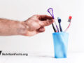 Hand reaching for a tongue scraper out of a cup of assorted dental tools