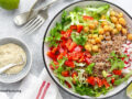 Round bowl of beans, greens, and other whole foods on a white surface