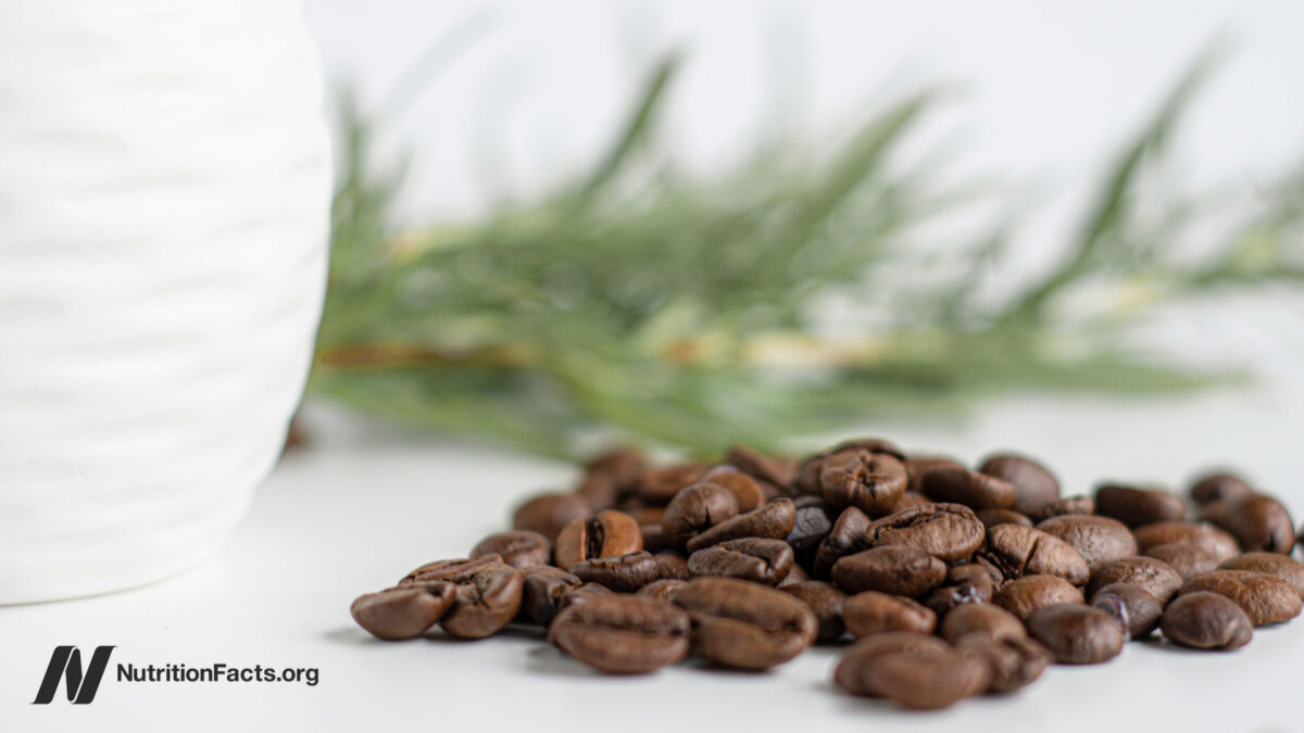 Coffee beans spilled on white with rosemary leaves in the background