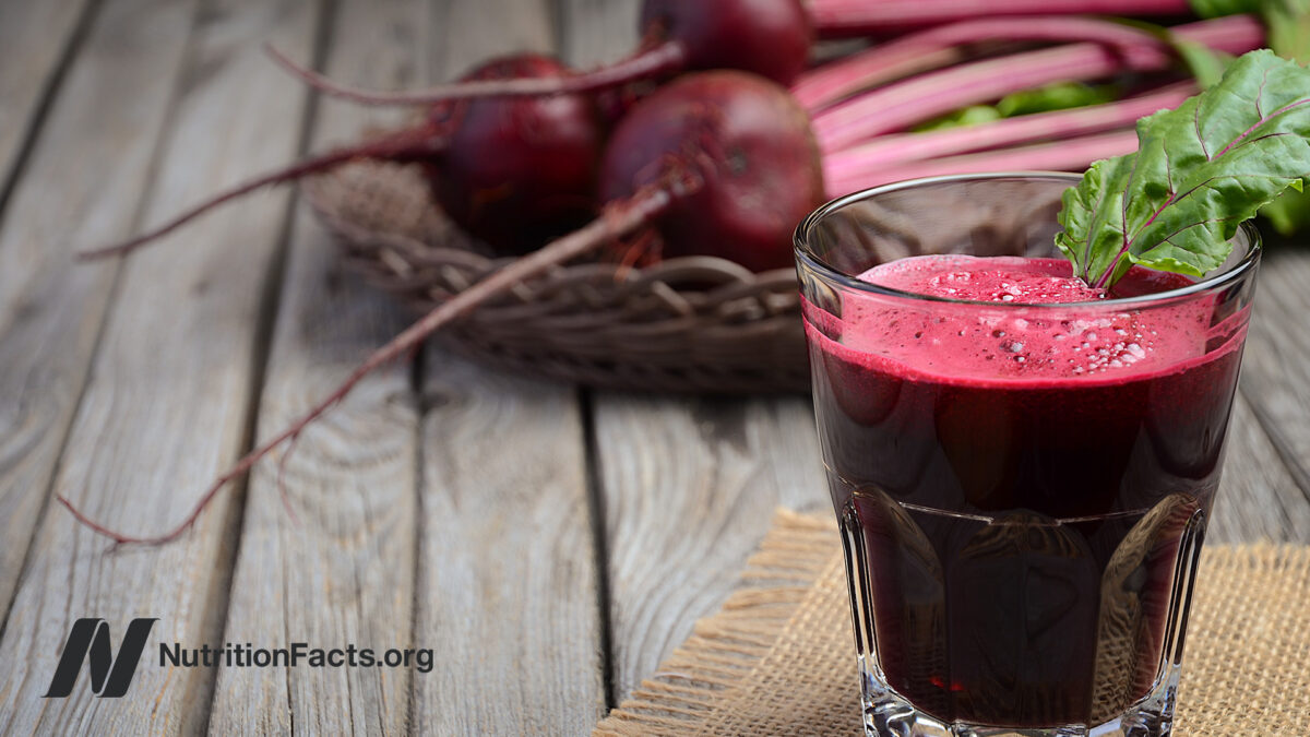 glass of beet juice with a basket of whole beets in the background