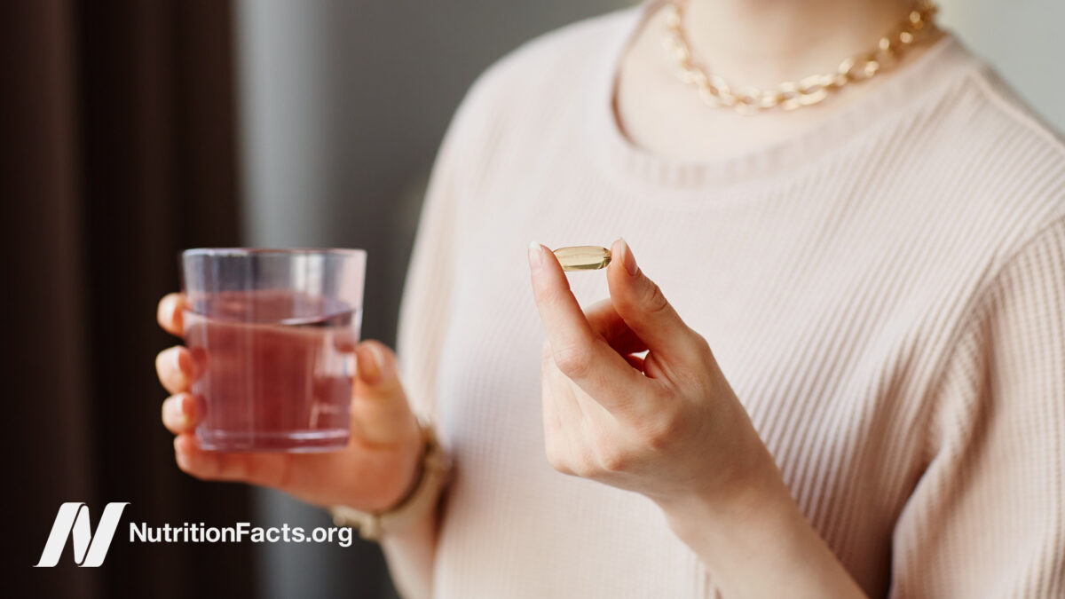 Person taking a supplement capsule with a cup of water