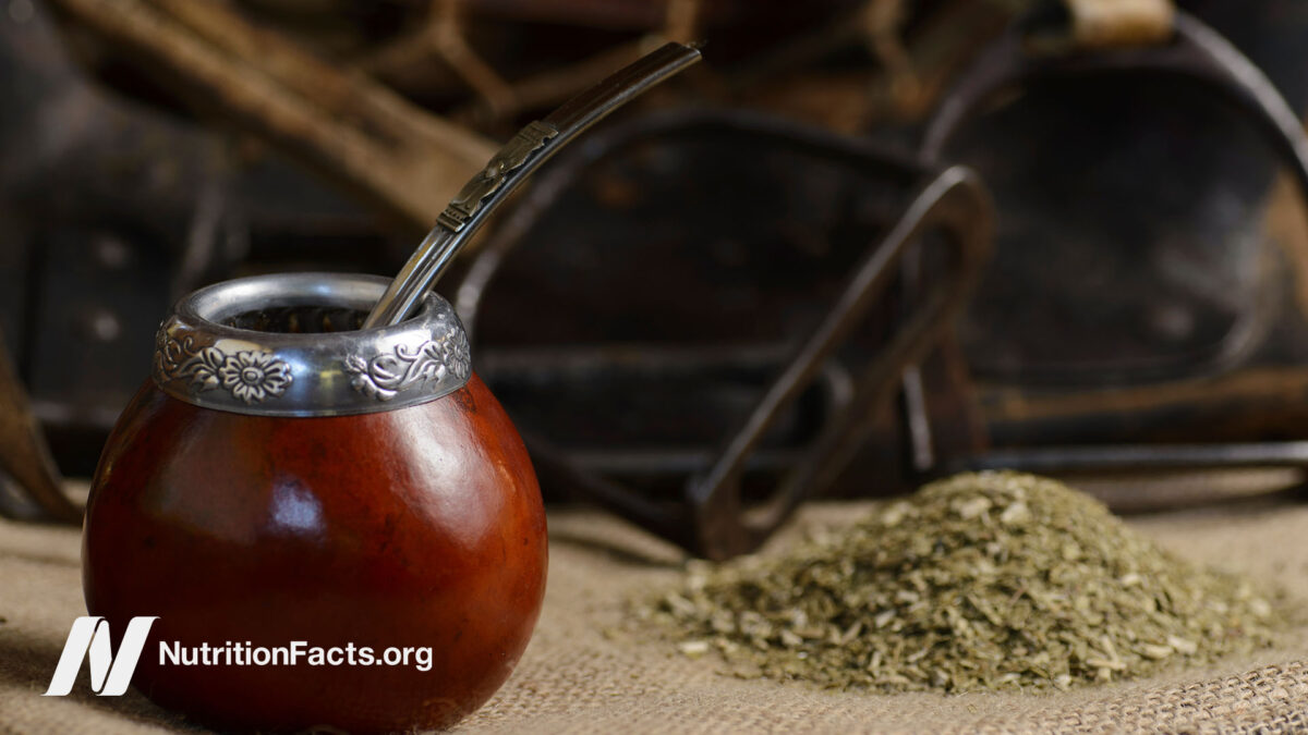 Close up view of a yerba mate gourd, also known as a bombilla, used to drink loose leaf yerba mate with a metal straw next to a small pile of yerba mate