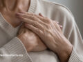 Elderly person wearing a sweater holding both hands to their chest