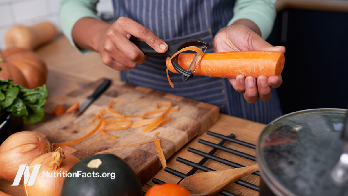 Person peeling a carrot in their kitchen surrounded by various vegetables