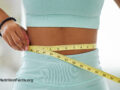 Person wearing teal workout gear measuring their waist with a yellow measuring tape