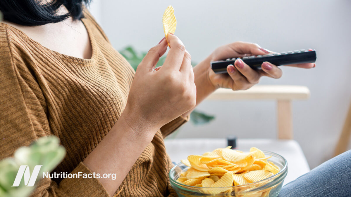 Side view of a person sitting on a couch with a bowl of potato chips on their lap