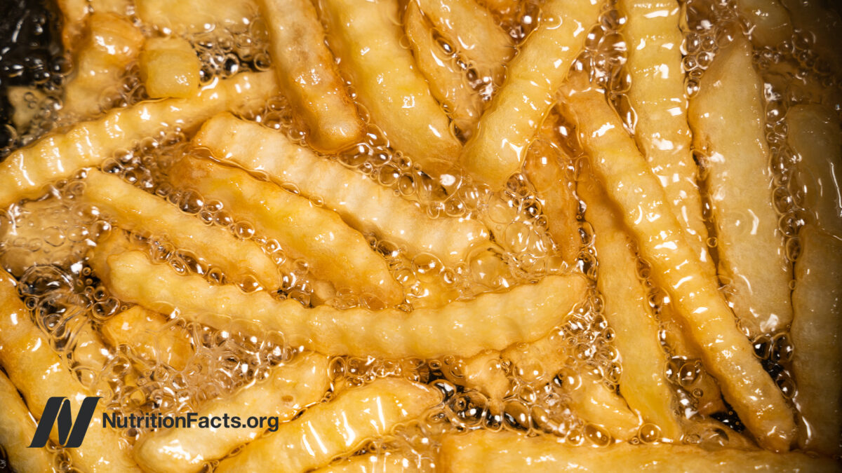 Closeup view of crinkle cut french fries submerged in bubbling hot cooking oil