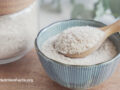 A glass jar of powdered psyllium husk next to a bowl of psyllium husk powder with a spoon inside