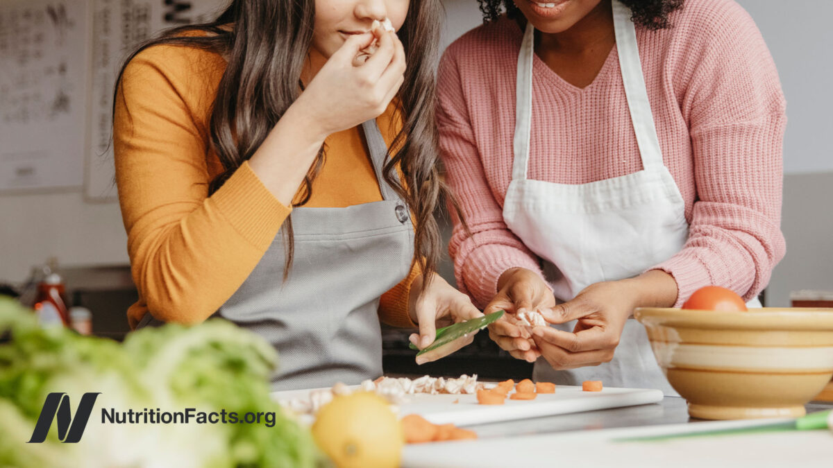 Two people cooking in a kitchen, with one person holding up herbs to smell