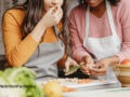 Two people cooking in a kitchen, with one person holding up herbs to smell