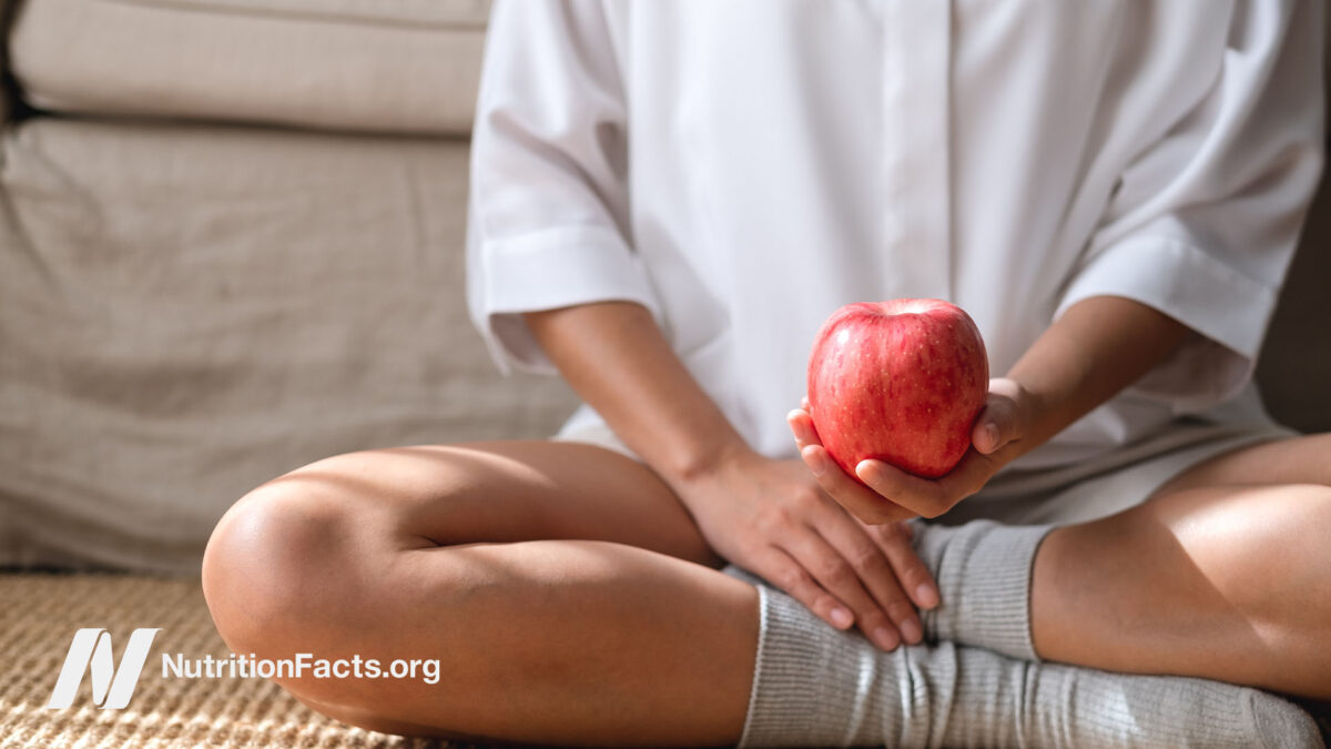 Person sitting on the ground holding a red apple