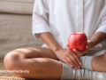 Person sitting on the ground holding a red apple
