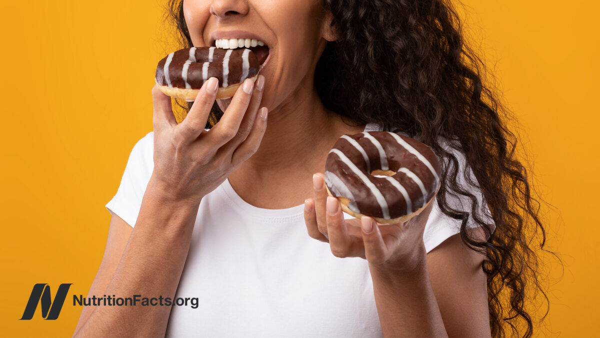 Person eating chocolate glazed doughnuts in front of a mustard yellow background