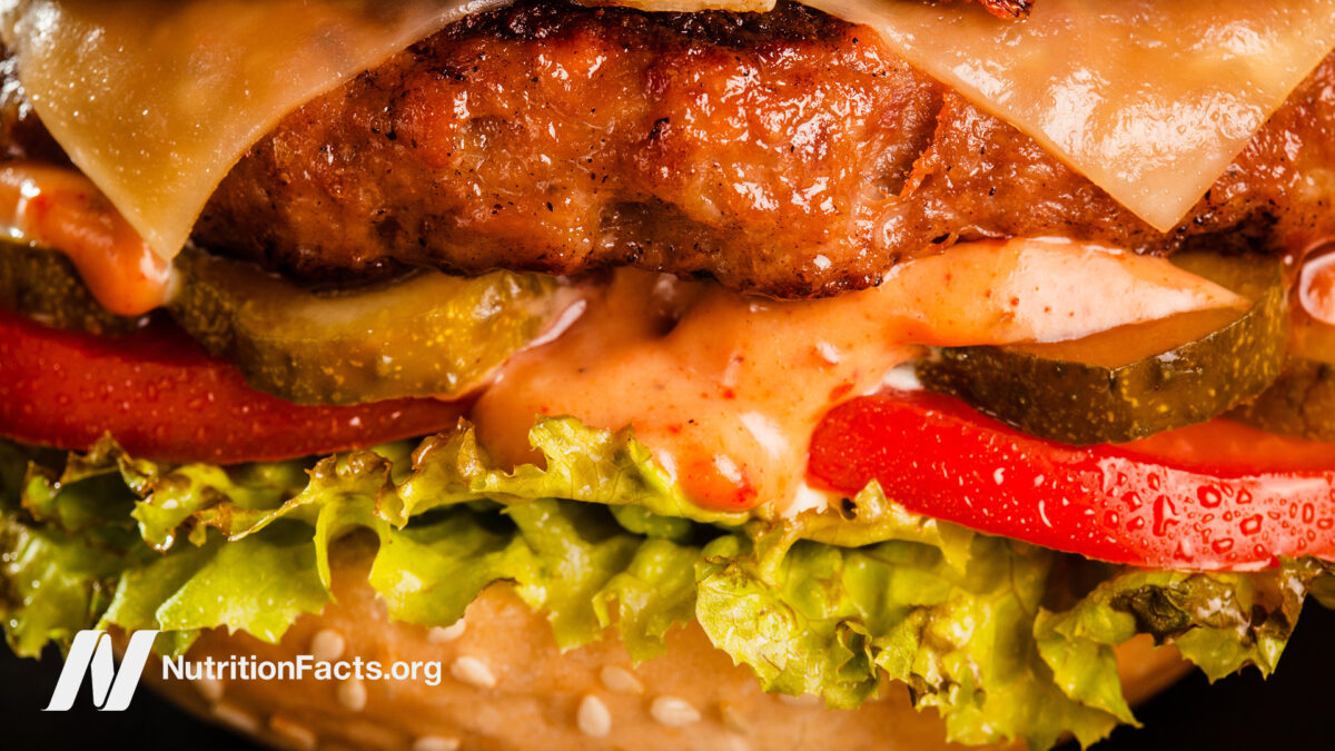 Close up macro view of a cheese burger with a sauce, pickles, tomato, and lettuce on a sesame seed bun