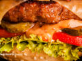 Close up macro view of a cheese burger with a sauce, pickles, tomato, and lettuce on a sesame seed bun