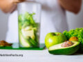 Person making a smoothie in the background with vegetables like kale and avocados