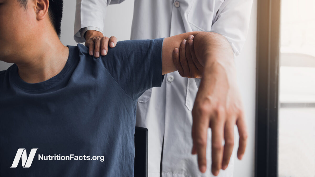 Physical therapist holding up a person’s arm and resting a hand on their shoulder