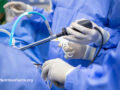 Surgeons in blue scrubs wearing gloves and holding surgical instruments during a procedure