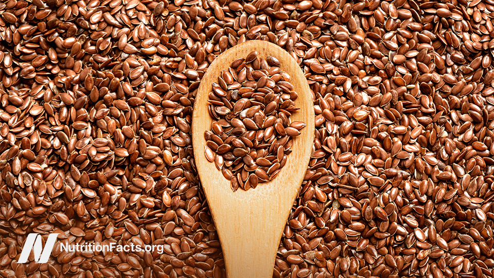 A wooden spoon full of flax seeds sits on top of a pile of flax seeds