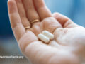 Closeup view of a hand holding two ibuprofen pills